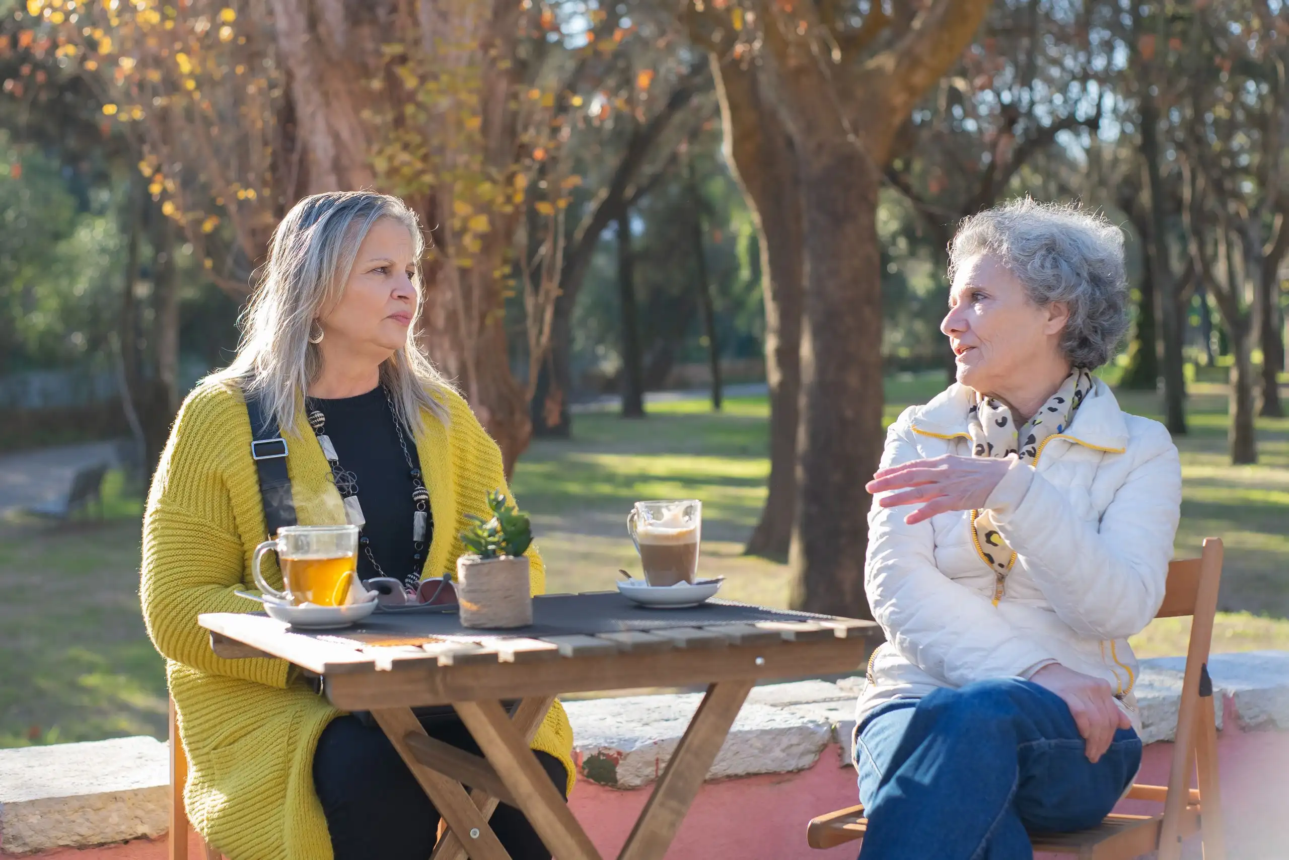 Two women talking over cups of tea at a table in a park